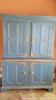 Front view of closed cabinet showing distressed blue paint and four paneled doors