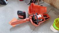 Open orange plastic case containing Stihl 026 chainsaw with bar cover, next to a jug of bar & chain oil
