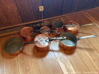 Overview of all copper pots laid on floor with wooden rod behind