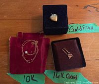 Overall photo of the three jewelry items: 10K gold chain with pearl bead on red velvet, 14K gold charm in a black box, gold filled heart-shaped locket pendant in a black box labeled 'Goldfilled'