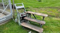 Overview of green hose reel with crank handle and attached red-and-black garden hose alongside three-step wooden ladder with dark wood steps on grassy lawn near greenhouse.