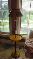 Full view of the tall vintage metal floor lamp with round shelf and large lampshade in front of window.