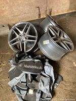 Four silver AMG wheels stacked on barn floor with branded storage bags.