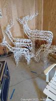 Four white wire‐frame reindeer sculptures grouped against wood wall