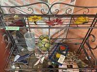 Full view of stained glass hanging pieces arranged on metal rack with mosaic glass vases and suction cup hangers.