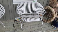 White bench and mosaic side table on wooden deck under window