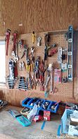 Full pegboard view showing a variety of hand tools hung by hooks above bins on ledge