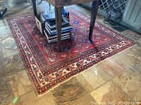 Full view of red geometric rug under table on stone tile floor
