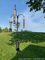 Three hanging tube bird feeders displayed outdoors on a tall black metal garden hook with a weighted base inserted into ground.
