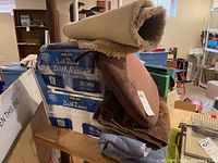 Photo of rolled bath rugs on top of folded towels and seat cushion with a pack of Kirkland bath tissue in background.