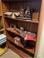 Shelf showing wooden ship-themed bookends, cast iron skillet with handle, wooden board, harmonica, and black decorative bowl.