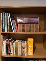 Books arranged on wooden shelves showing various titles including large dictionaries and smaller gardening and travel books.