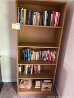 Full bookshelf with four shelves mostly filled with books and some boxes at the bottom.