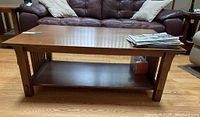 Photo of oak mission style coffee table showing top surface, scratches and water stains, lower shelf and slatted wooden sides.