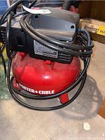 Side view showing red cylindrical tank, Porter-Cable label, black motor housing, hose coiled on top