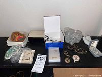 Photo showing assortment of costume jewelry including cuff links, necklaces, beads, pendants, and jewelry boxes arranged on a surface.