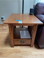 Front view of one oak mission style end table with drawer and slatted sides, showing wood grain and wear on corners.