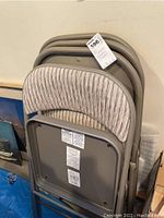 Stack of four padded folding chairs with striped fabric upholstery on seat and backrest, gray metal frames.