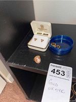 Photo showing all items including the cameo ring, two blue dishes holding the gold earrings and the jewelry box, and auction tag showing the lot description of 10k and 14k gold ring and earrings.