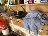 Wider view of shelf containing plastic organizers, hand clamps, cleaning rags, plumbing snake coil, and drawer liner roll