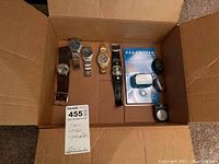 Box containing 6 men's watches and 3 pedometers/step counters arranged inside a cardboard box.