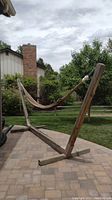 Full view of rope hammock suspended on wooden stand on paver patio outdoors.