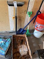 Image showing adjustable outfeed roller against wall with yellow handle and metal roller bar, alongside yard tools (shovels and bucket) and box of hand tools on floor, including files, rasps, and small parts.