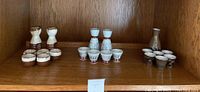 Three separate ceramic sake sets on wooden shelf with varying cup quantities and colors.