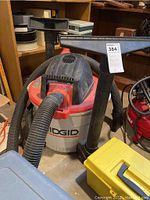 Photo of the Rigid shop vacuum showing red and white bucket base and black motor top with hose attached and large floor nozzle attachment.