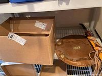 Photo showing cardboard box and a large round copper plate with decorative marks on the edge