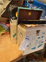 Two vintage metal storage boxes containing numerous 45 RPM vinyl records from the 60s-70s era placed on a wooden table. One box lid open showing stacked records.
