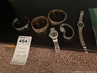 Photo showing six assorted women's jewelry items including bracelets and watches on a dark surface.