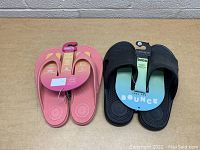 Photo of two pairs of Totes brand sandals, one pink women's flip-flop and one black men's slide style, both new with tags and packaging.