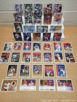 Front view of a collection of 43 NFL football cards laid out on a table with some arranged on a white display stand showing multiple players and different card styles.