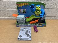 Overview of Hot Wheels City Toxic Creatures toy set with figure, launcher, car, and manual on a brown surface against a brick wall.