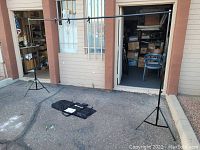 Full view of the assembled Esker backdrop stand showing two tripods and horizontal support bar outdoors near building entrance.
