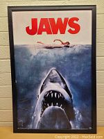 Front view of framed JAWS poster with shark and swimmer artwork showing the red JAWS title at top and black frame.