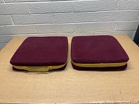 Top view of two maroon and brown seat cushions placed side by side on a table, one with a yellow handle