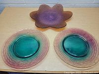 Top view of two round colorful glass platters and one flower-shaped purple glass platter on a table.