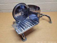 Angled side view of hand crank deli slicer showing blade, base, and legs