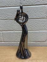 Front and side photos of the highly reflective chrome statue showing the man and woman figures embracing within a circular frame holding a heart shape.