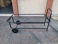Diagonal front side view of the black metal garbage can caddy cart with two wheels and one handle.