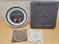 Porcelain plate standing on easel with certificate booklet and protective foam packaging beside it.