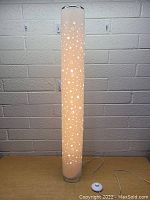 Front view of tall cylindrical floor lamp lit with star cutout pattern visible