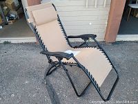 Full side-angle view showing chair reclined position, beige fabric stretched by black elastic cords on black metal frame with armrests and cushioned headrest.