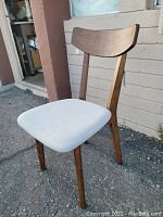 Front-right angled view of wooden accent chair with light upholstered seat cushion, showing backrest and seat details.