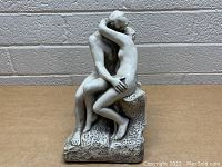 Front view of vintage sculpture depicting a man and woman nude embracing on a rock-like seat.