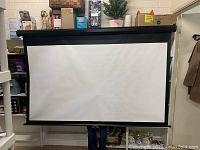 Front view of white projection screen extended from black casing, mounted against a wall, displayed fully extended with visible black border edges.