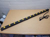 Image showing full length of the long black metal power strip with twelve yellow outlets in a row, laid flat on a wooden surface.
