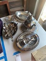 Overview of various silver serving pieces including platters, tea pot, silverware in bowls showing tarnish and wear.